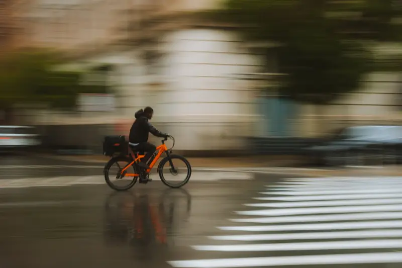 Cyclist riding through a wet city street in the rain, spray coming off the road